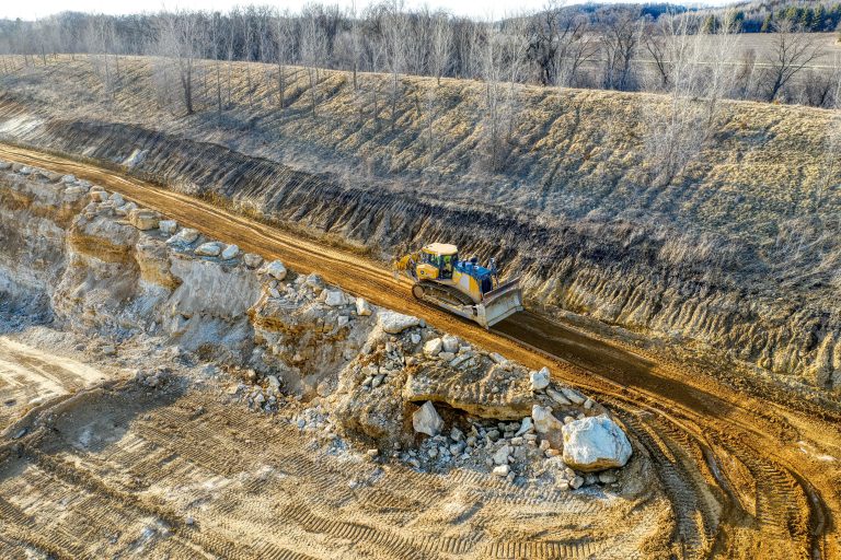 An aerial view of a bulldozer operating on a rocky terrain in a quarry setting during daylight.