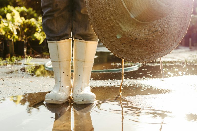 A person wearing rubber boots and a hat standing in a puddle