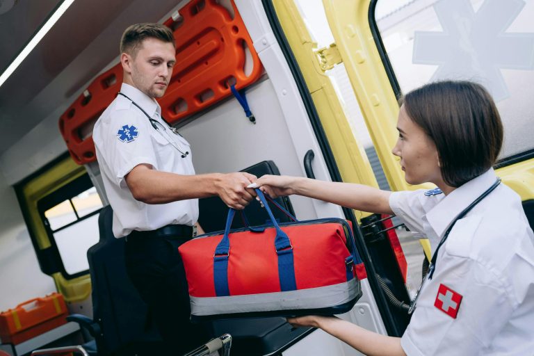 Male and female paramedics exchanging a medical kit inside an ambulance, showcasing teamwork.