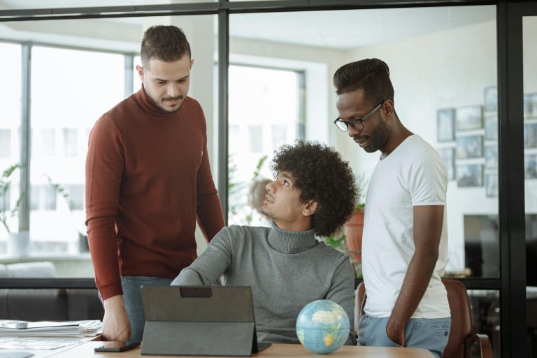 Three colleagues discussing a project with a laptop and a globe in a modern office setting.