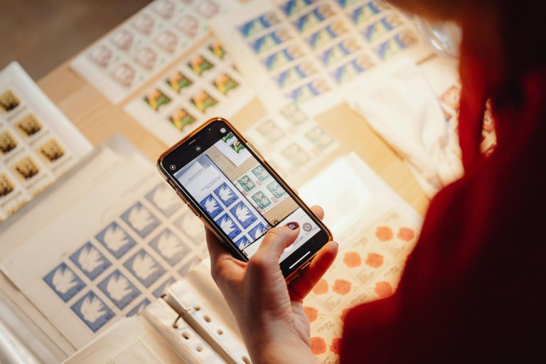 A person uses a smartphone to photograph a detailed stamp collection on a table.