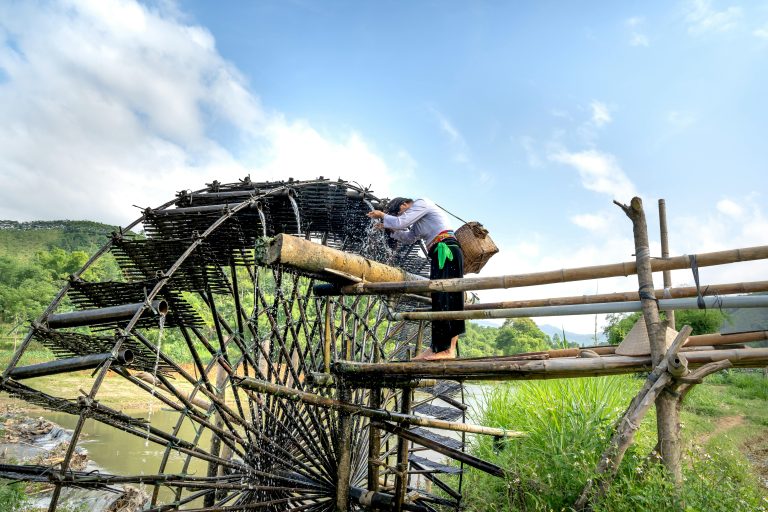 Full body side view of female with basket washing hair in water mill in rural town