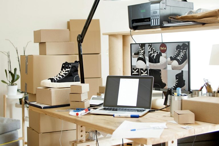 A busy workspace with sneakers, boxes, and a laptop indicating an online shoe store or e-commerce setup.