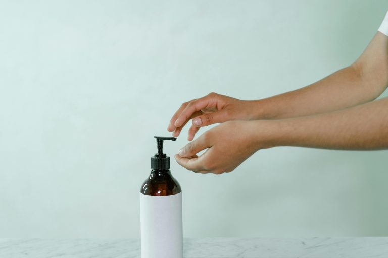 A minimalist photo of hands reaching for a pump bottle with a blank label on a white background.