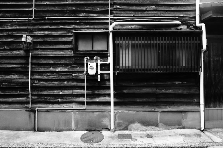 Grayscale image of a rustic wall with exposed pipes, depicting vintage urban architecture.