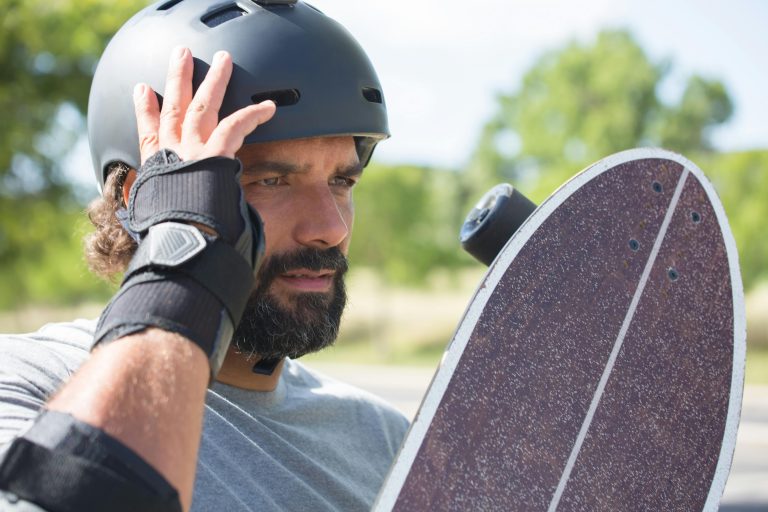 Adult male skater adjusting helmet while holding a skateboard outdoors, focusing on safety and protection.